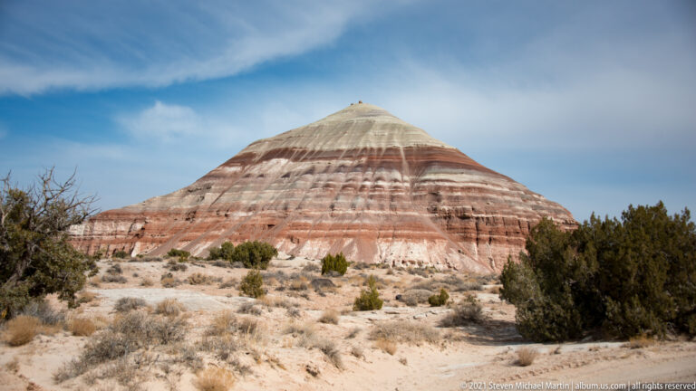 A banded conical sandstone butte rises above sparse scrub beneath a clear sky.
