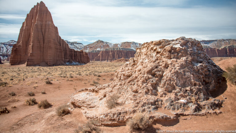 A large pale boulder fills the foreground while a tall red sandstone monolith rises behind it at left.