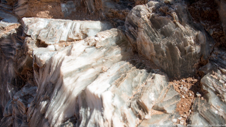 Pale mineral veins and fine cracks cross angular brown rock in a close geological detail.