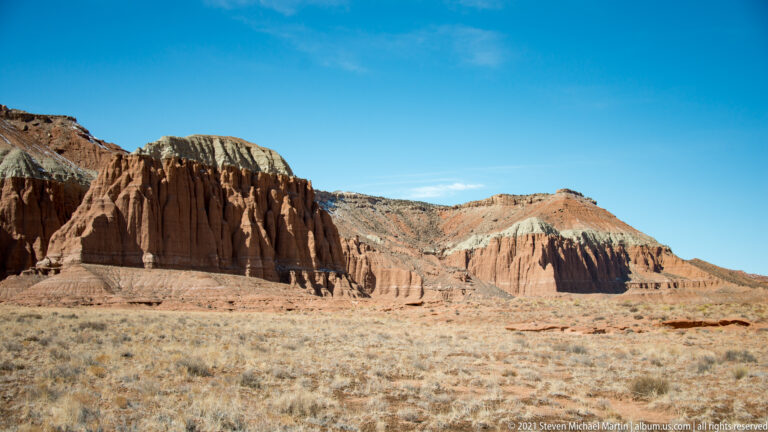 Layered red, gray, and pale cliffs extend above a broad plain dotted with scrub.