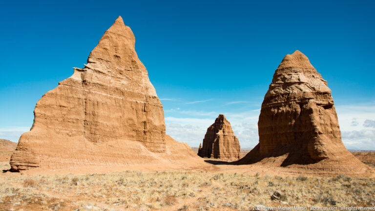 Three sandstone towers stand across an open grassy plain, with a smaller monolith between two larger ones.