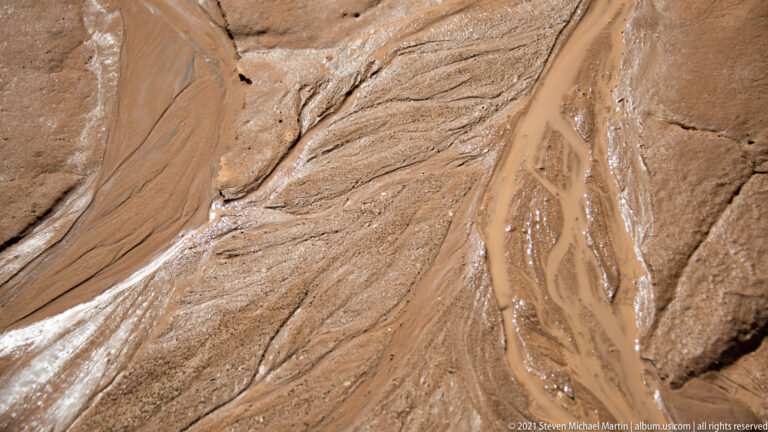 Fine parallel lines follow a rippled sandstone surface, with a small dark patch near the lower edge.