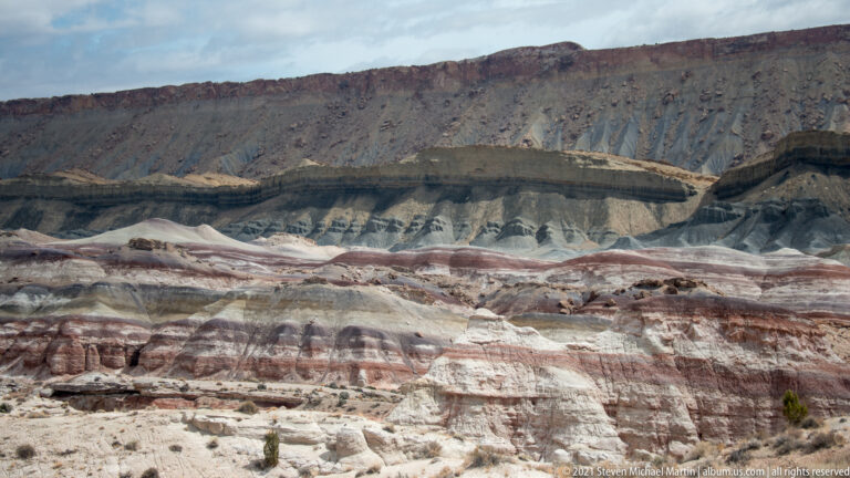 Gray gullied slopes cut across a cliff face banded in pale and rust-red layers.