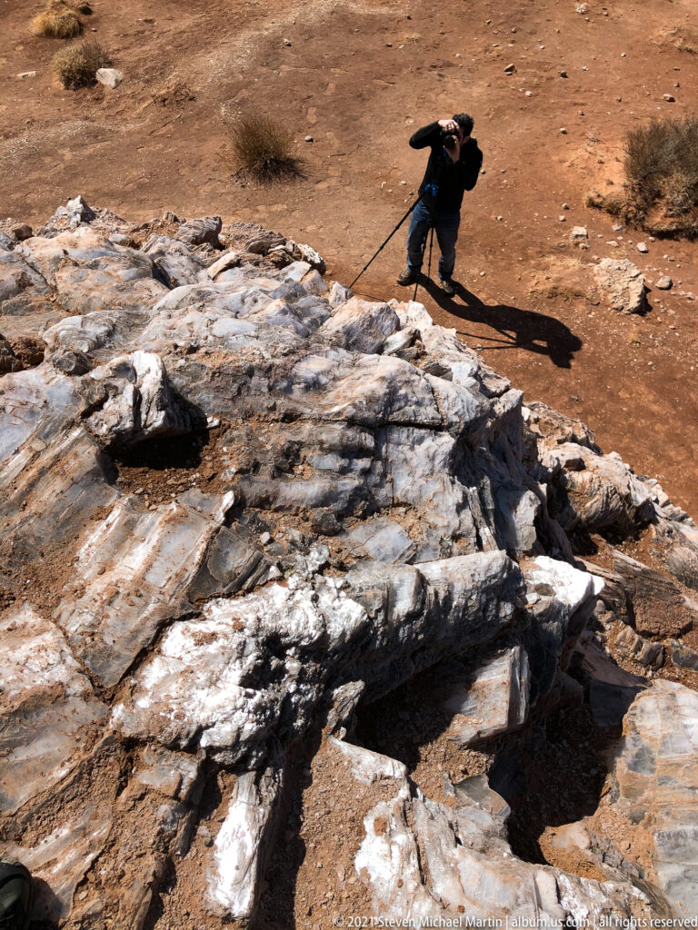A photographer bends over a pale rock outcrop with a tripod on reddish ground.