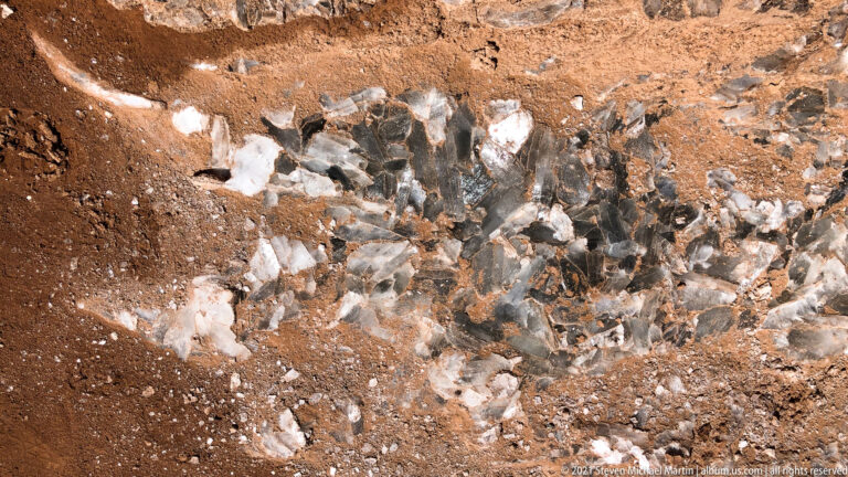 White and gray angular seams cut through red-brown soil in a close geological detail.