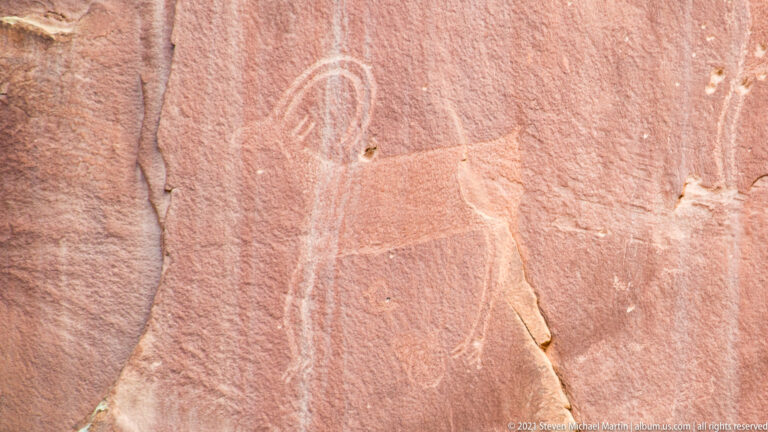 A faint elongated figure is outlined on a close view of a red sandstone surface.