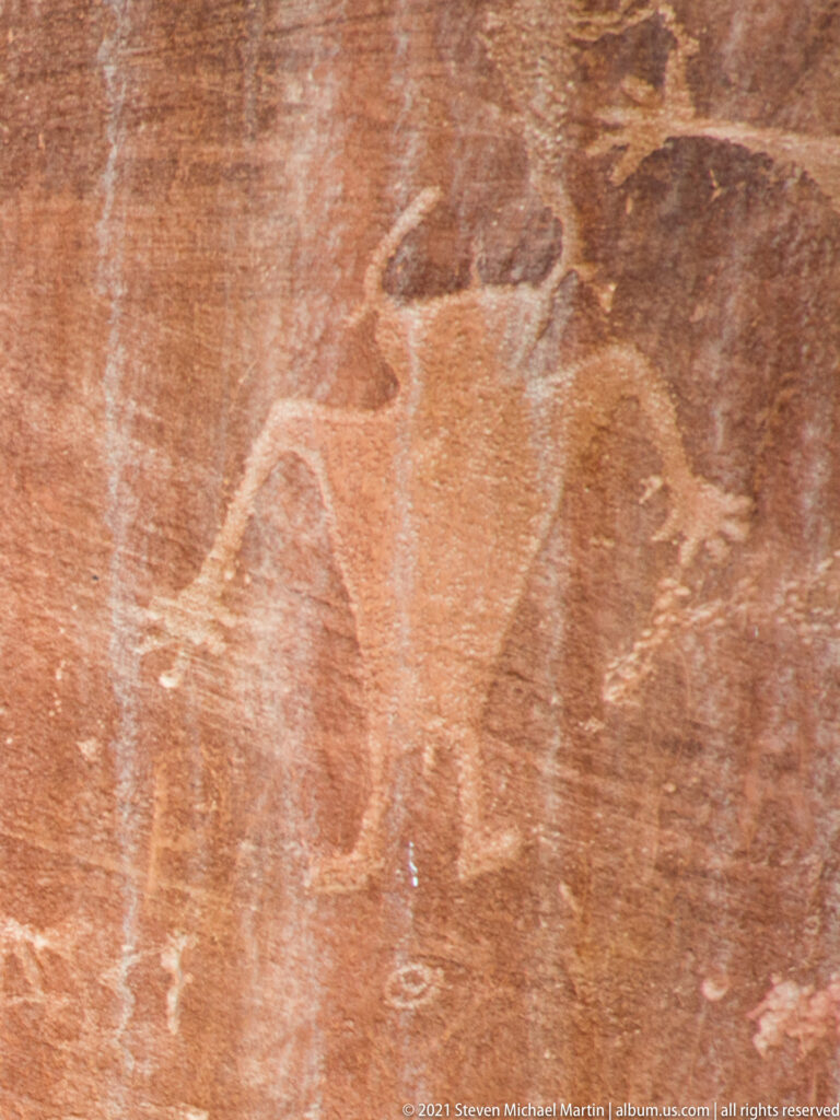 A faint animal-like outline appears on weathered red sandstone above a pale rock ledge.