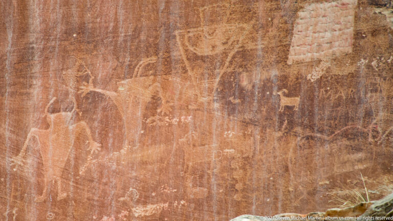 Faint human-like figures and a small animal outline appear across a red rock panel.
