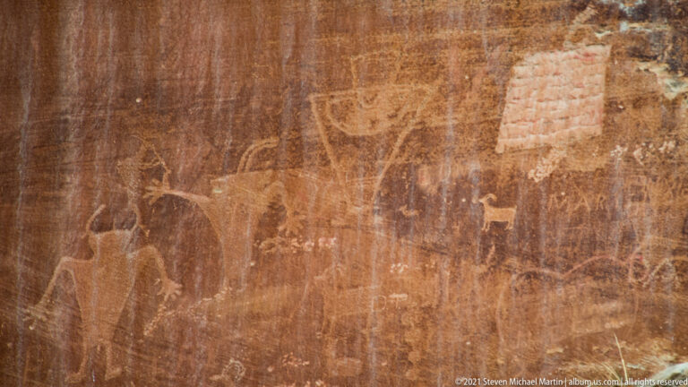 A small quadruped outline appears among larger pale figures on a red sandstone panel.