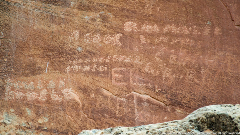 Faint pale marks and an indistinct figure cross a close view of red sandstone.