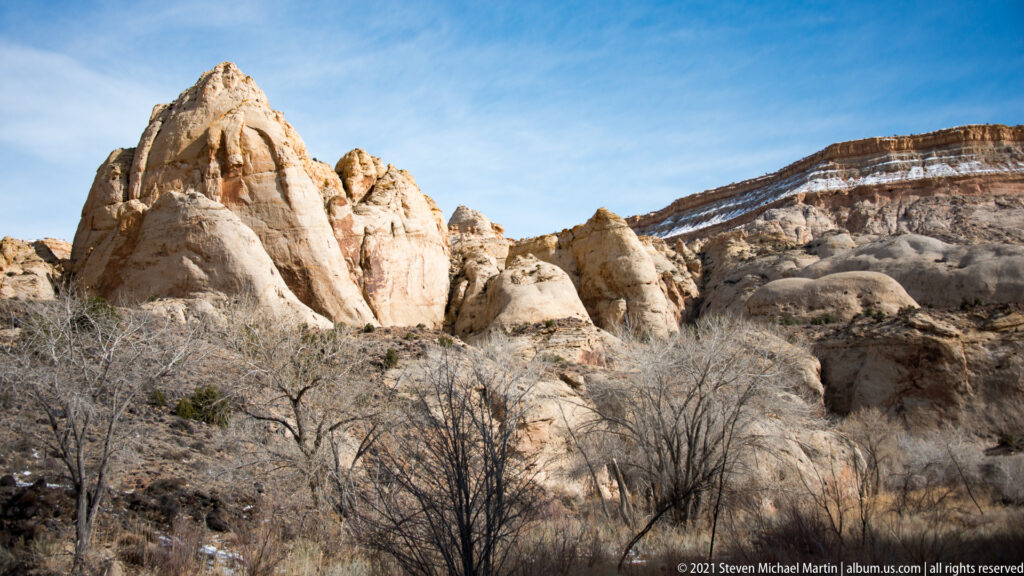 Rounded pale sandstone towers stand above scrub beneath a long dark ridge.