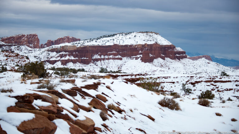 A flat-topped mesa with horizontal red and pale rock bands rises above snowy ground.