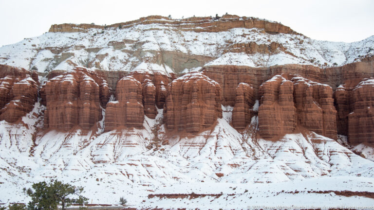 Rounded red-rock ribs repeat across a snowy slope beneath a pale upper ridge.