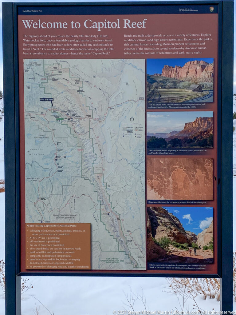 A framed Capitol Reef information panel displays a map, landscape photographs, and visitor guidance above snow.