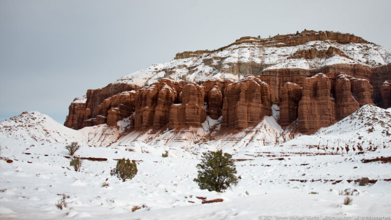 Rounded red sandstone columns stand above a snowy slope beneath a layered ridge.