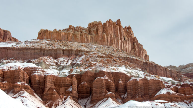 Jagged red sandstone towers rise above snow-streaked slopes and rounded lower columns.
