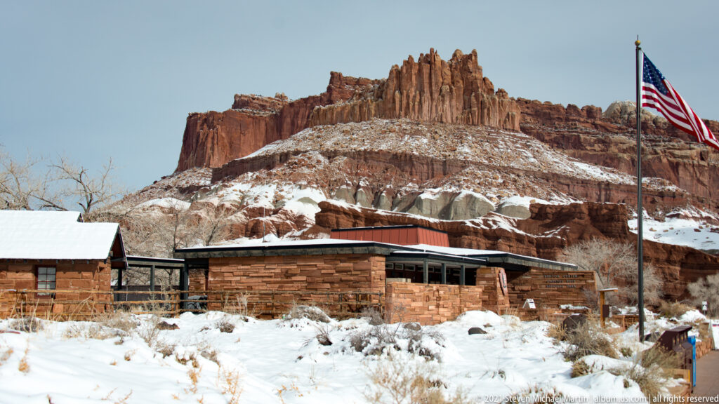 The stone visitor center and a United States flag stand below the red sandstone Castle formation.