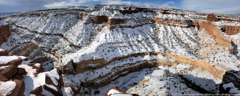 Snow traces the shelves and slopes of a deep, curving canyon seen from its rim.