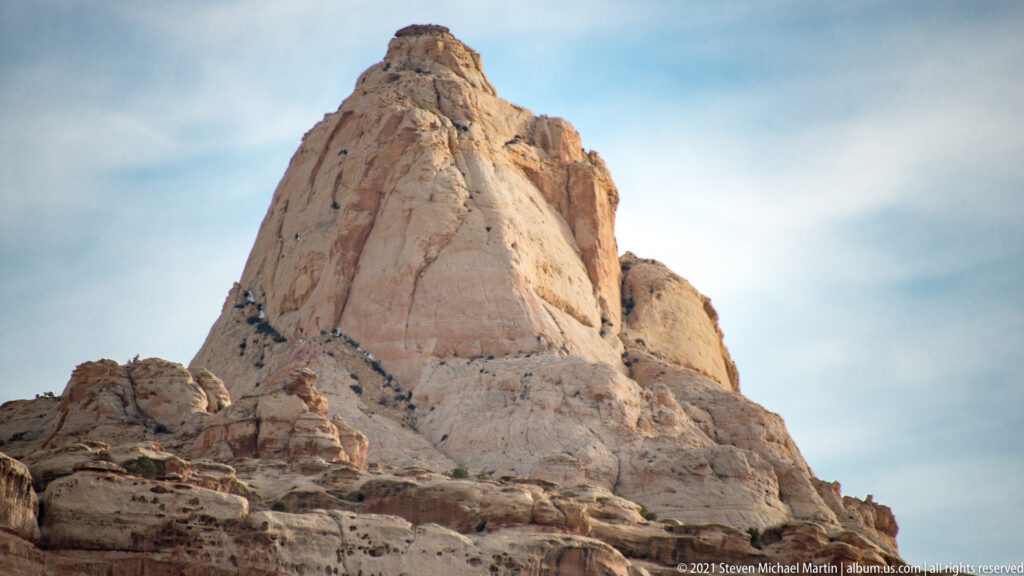 A rounded pale sandstone peak rises sharply above layered slopes against a light sky.