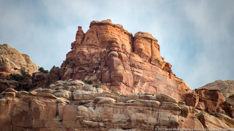 A blocky red sandstone tower rises above pale ledges beneath a cloudy sky.