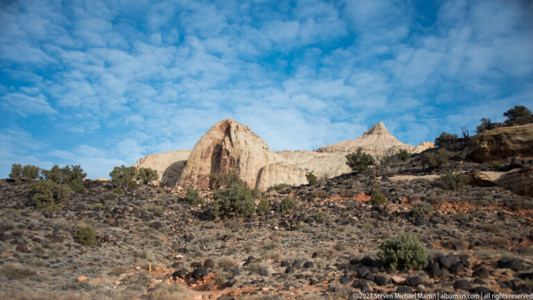 Two pale sandstone peaks stand above dark scrub beneath a broad cloud-filled sky.
