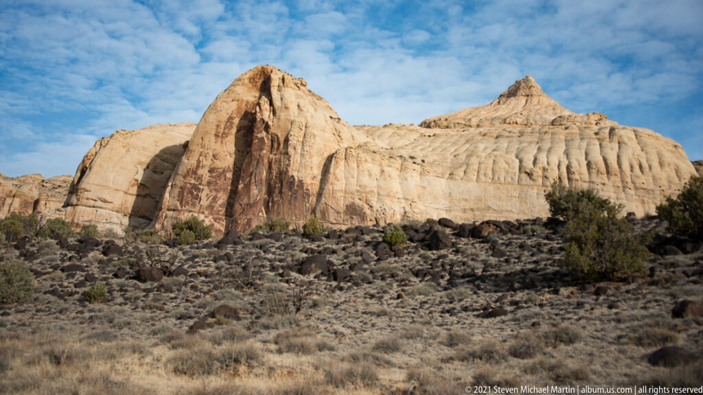 A broad pale peak and a sharper summit rise above a ribbed ridge and dark shrubs.