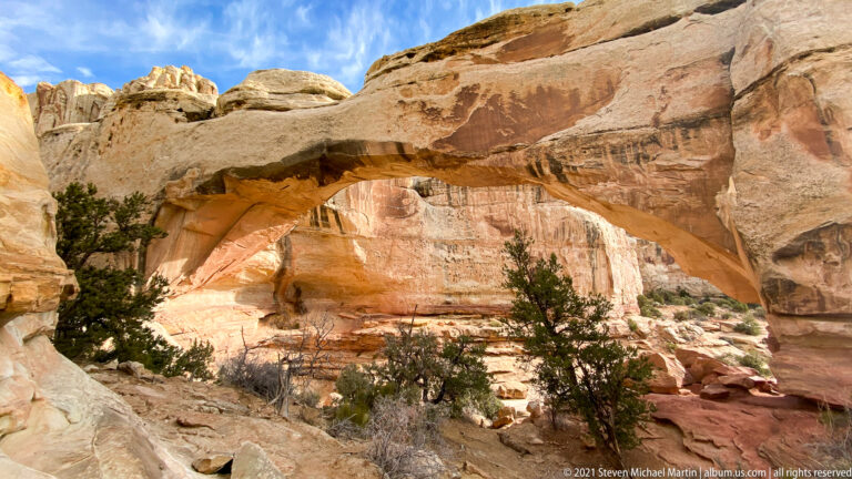 Hickman Bridge spans a broad rocky alcove above junipers and scattered boulders.
