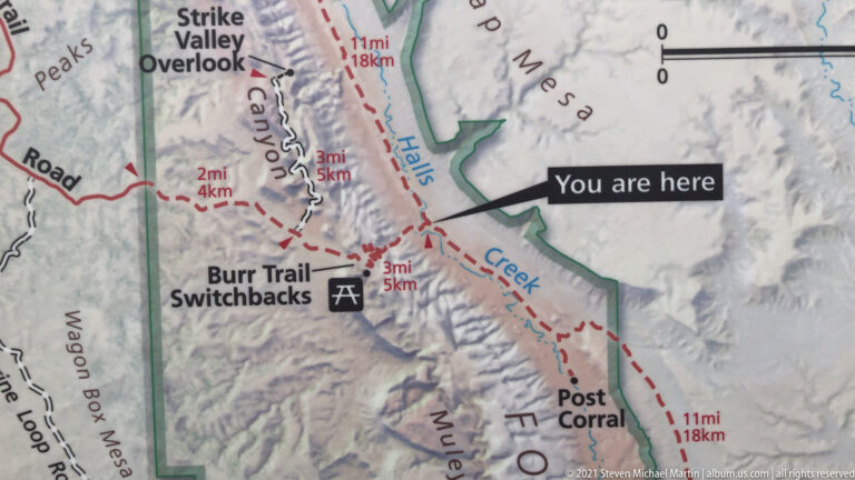 Printed map with a “You are here” pointer beside Halls Creek, the Burr Trail switchbacks and red dashed roads.