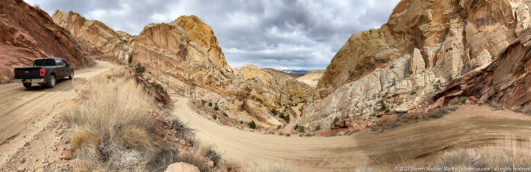 A dark pickup truck rounds a tight dirt-road bend between steep sandstone walls.