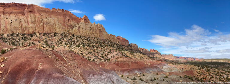 Long pale and red cliffs recede toward distant pinnacles above rounded foreground hills and a broad valley.