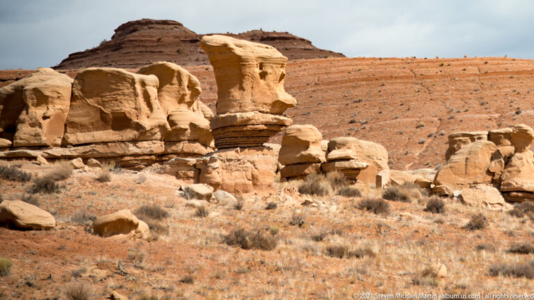 Rounded tan sandstone blocks and pedestal forms stand below a flat-topped ridge.