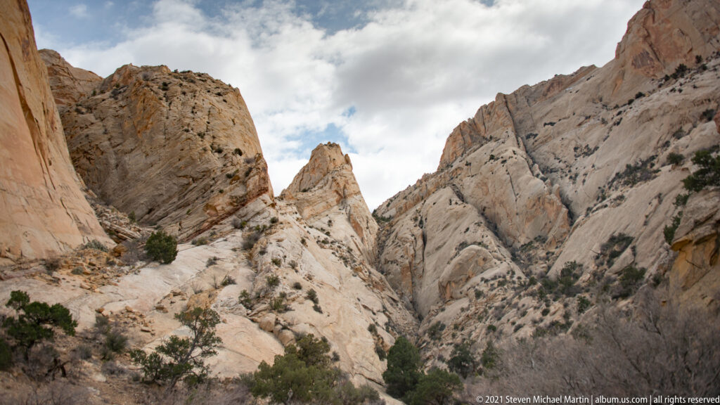 A pale rock pinnacle rises in a narrow gap between steep canyon walls beneath clouds.