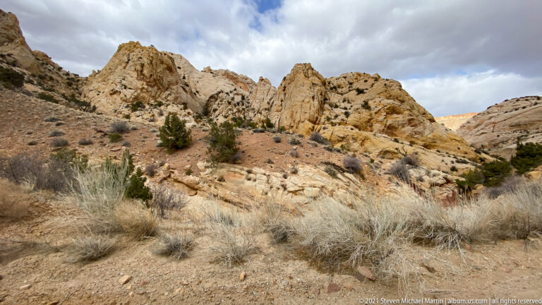 Wide view of pale sandstone towers above dry grass and scattered shrubs on a hillside.