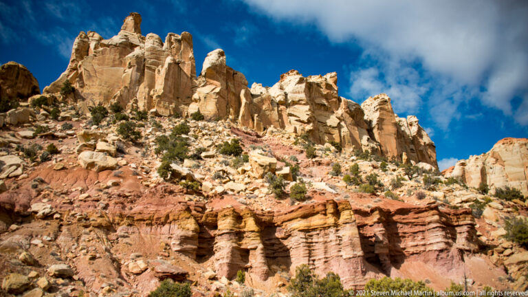 Pale sandstone towers rise over a red and cream cliff face carved into narrow fins and recesses.