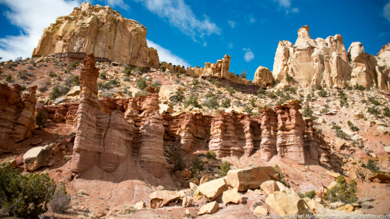 Red ribbed sandstone columns stand below pale towers, with broken blocks scattered at their base.