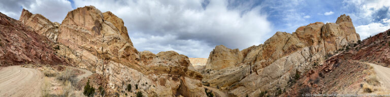 Pale road bends down between steep, closely spaced sandstone walls beneath a cloudy sky.