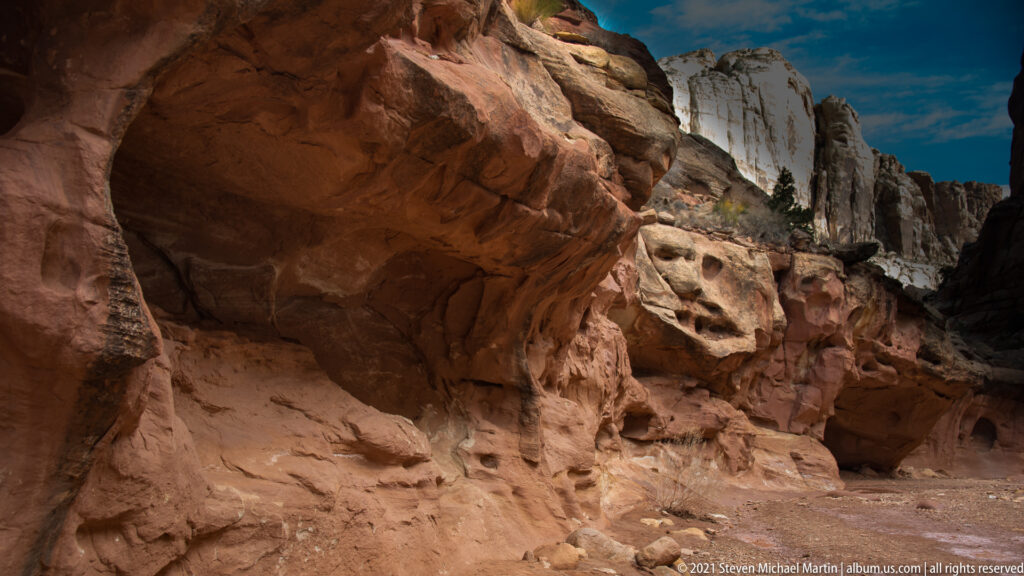 A massive sandstone ledge shelters a dark recess, with pale cliffs visible through an opening beyond.