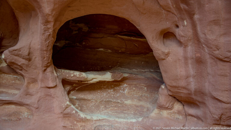 A large shadowed cavity sits beneath a rounded sandstone rim beside a smaller circular hollow.