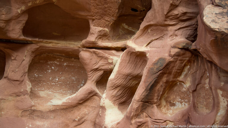 Curved red sandstone ledges and pale bands surround several dark recesses, divided by a narrow rock rib.