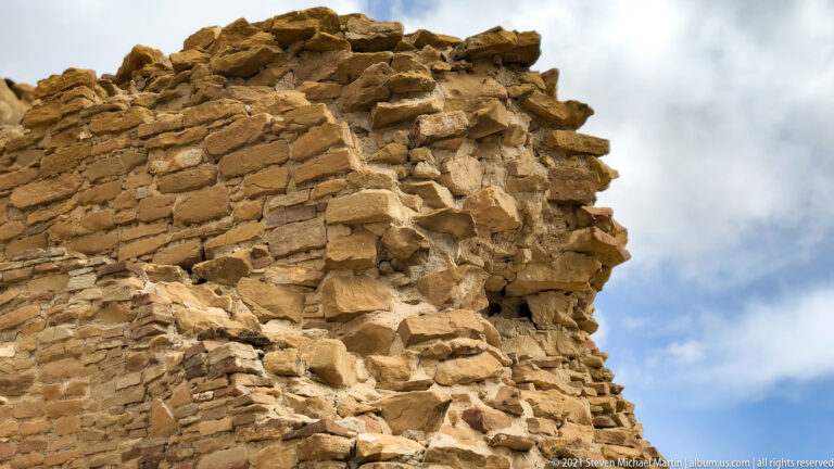 A stacked stone wall ends in a jagged, broken edge against a cloudy sky.
