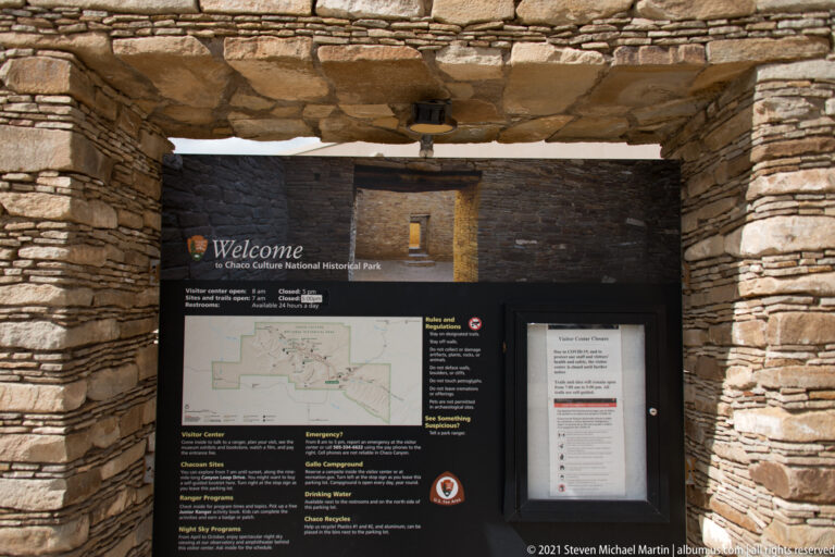 A black welcome panel with maps and visitor information fills a stone-framed opening at the park entrance.