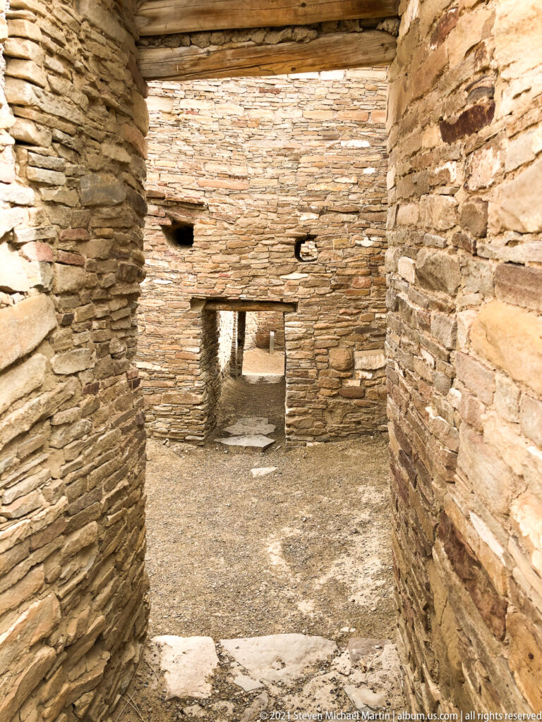 A narrow passage between high stone walls leads toward a small rectangular opening.