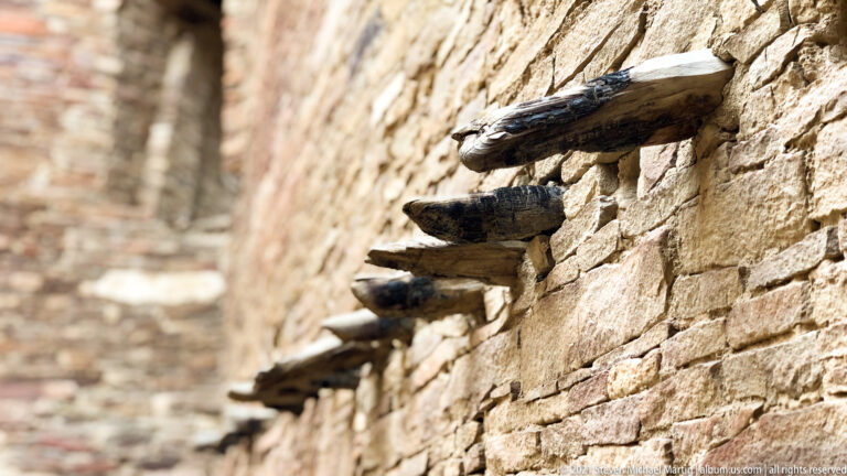 Dark rounded forms sit on projecting ledges along a stone wall, with the background softly blurred.