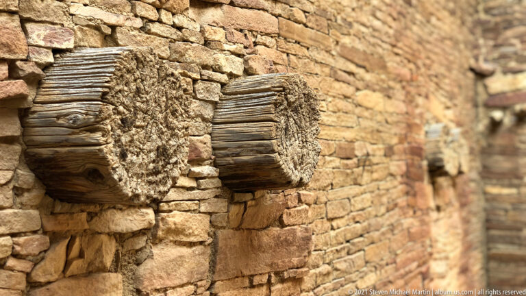 Two weathered timber beam ends project from a rough sandstone wall in close view.