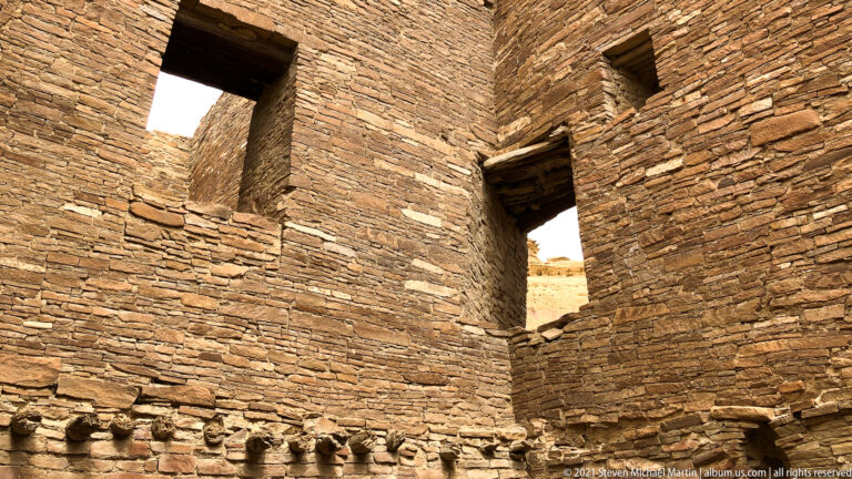 Tall masonry walls meet at a corner with narrow high openings and wooden lintels.