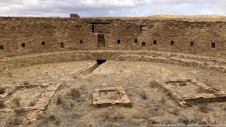 A circular stone enclosure contains a low rectangular feature and other masonry outlines across its floor.