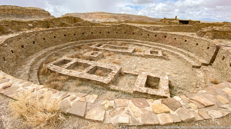 An overhead view shows a circular masonry enclosure containing several rectangular structures and smaller features.