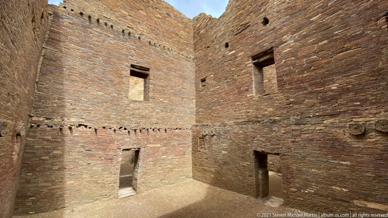 Tall stone walls meet at a corner, with small upper openings and doorways at ground level.