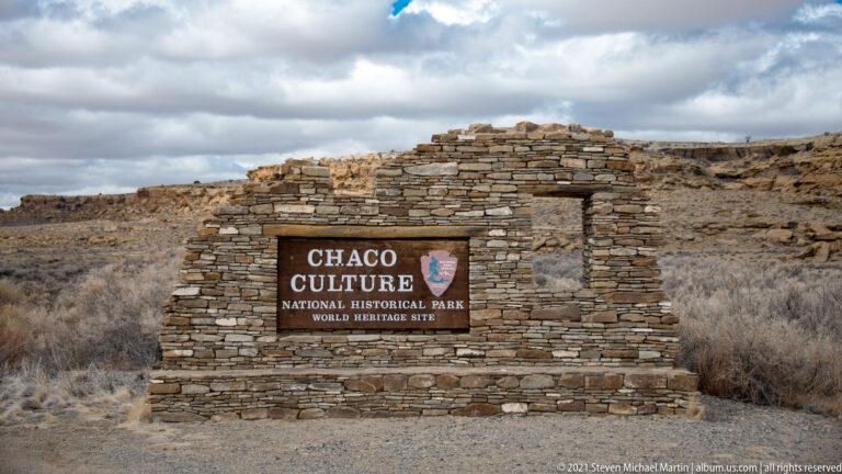 A stone sign identifies Chaco Culture National Park and its World Heritage designation in a scrubby desert landscape.