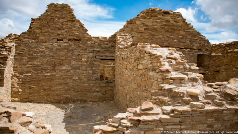 Standing stone walls enclose a court, with a lower stepped wall and small door openings in the foreground.